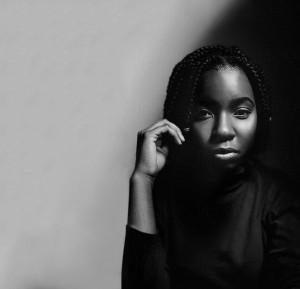 A young Black woman stares into the camera stoicly. 