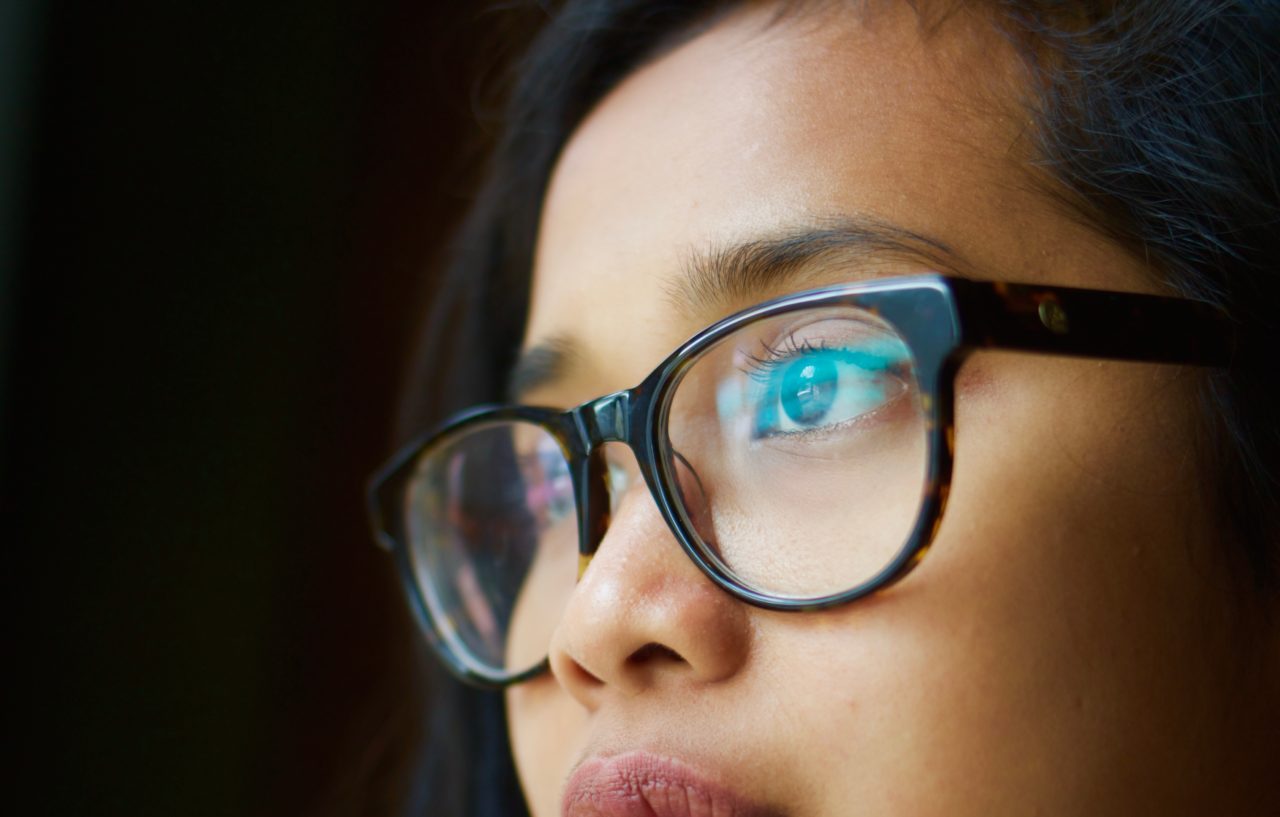 Racialized girl with big framed glasses gazing away from camera, cropped from lips to forehead.