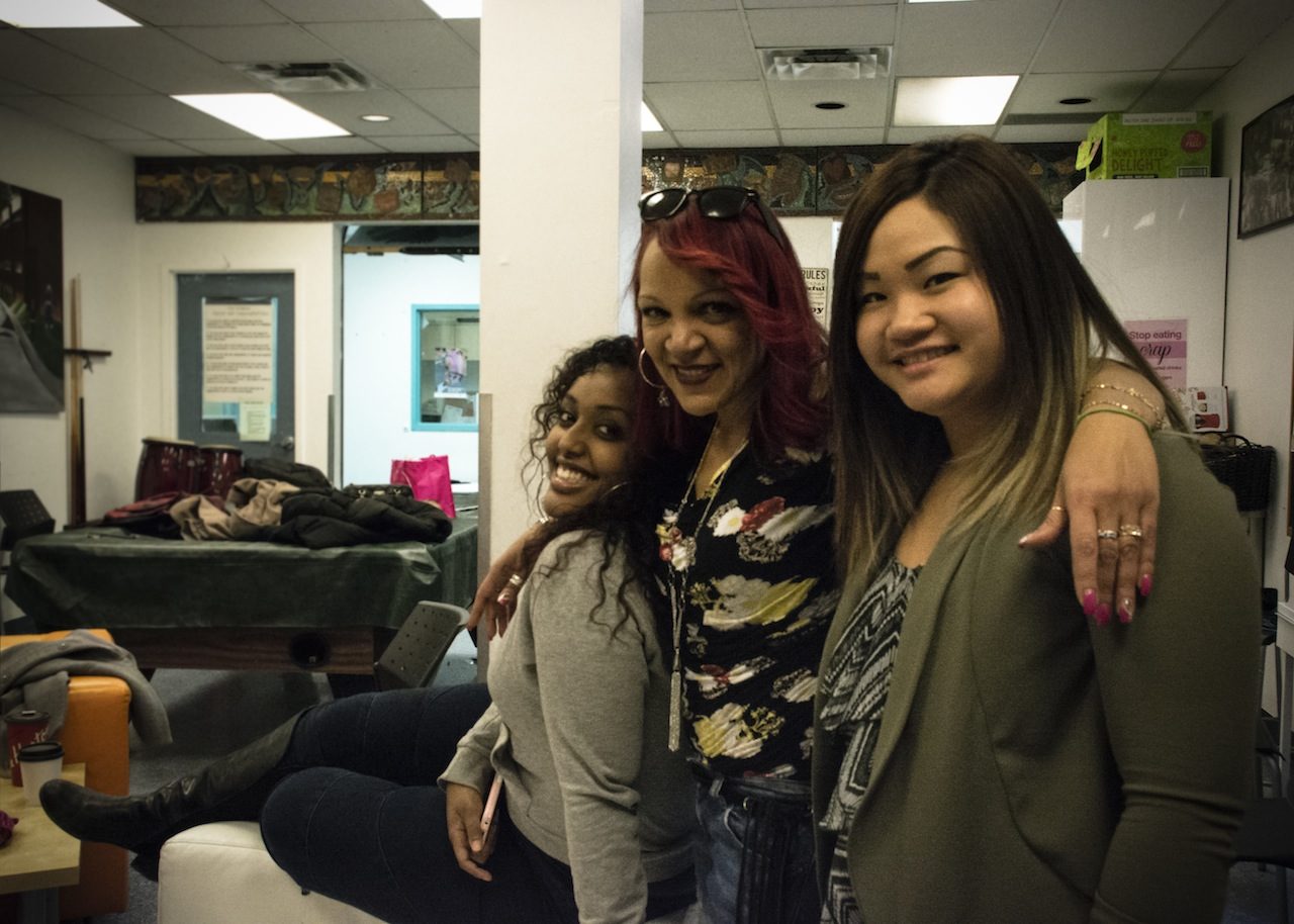 Diverse group of three women embracing and smiling at camera.