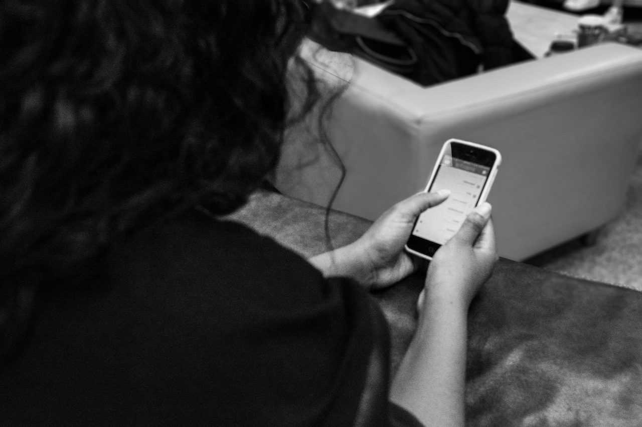 Photograph of racialized woman from behind as she looks at her phone screen messages. 