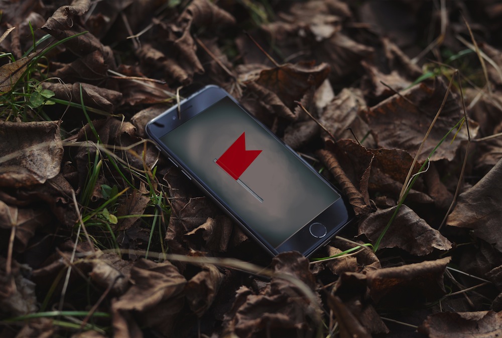 A phone abandoned in a pile of leaves depicts a red flag on the screen.