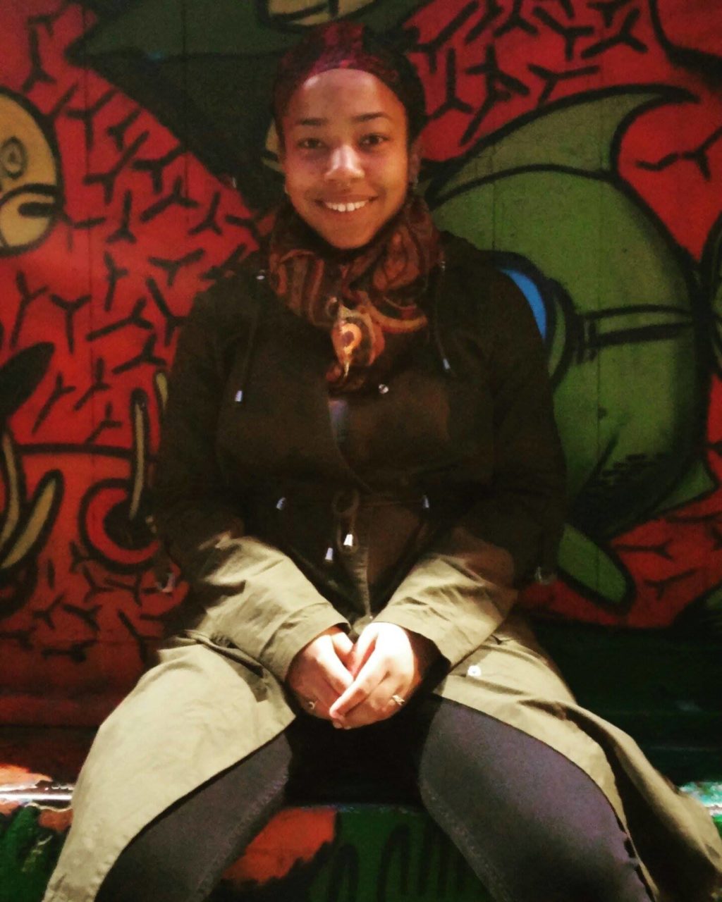 Jade posed and smiling in front of a graffiti wall. 