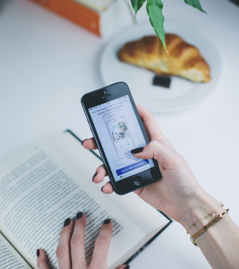 A woman's hand holding her phone, browsing the Tinder app over breakfast. 