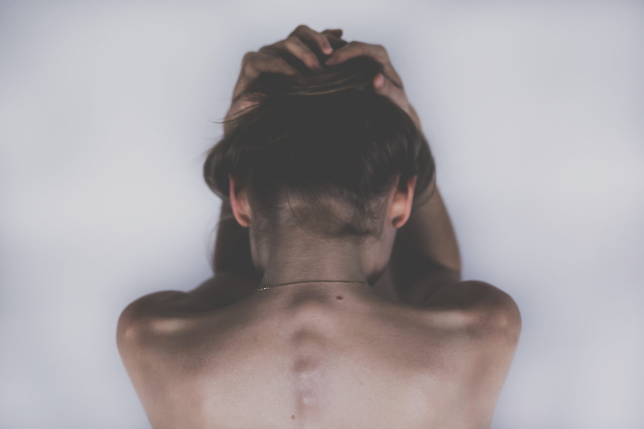 A woman crouches over with her hands above her head and her back exposed. 